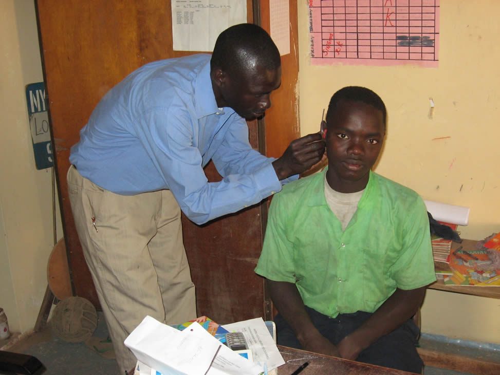 Itinerant Teacher Andrew Jatta fitting hearing aid to pupil in mainstream school